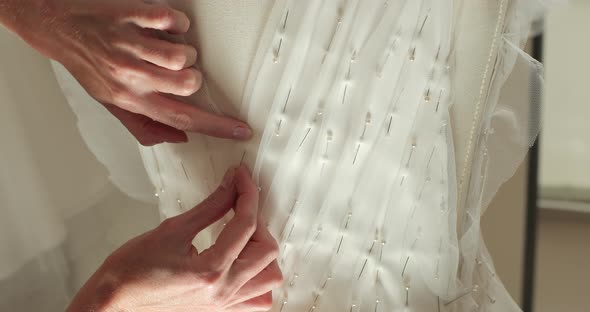 hands of a seamstress sticks pins into the corset  wedding dress on a mannequin