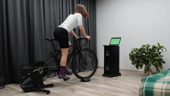 Indoor Virtual Cycling, Fit cycling woman rides bicycle at home on stationary bike out of saddle