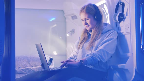 Young Woman is Listening to Music in a Capsule Hotel Room