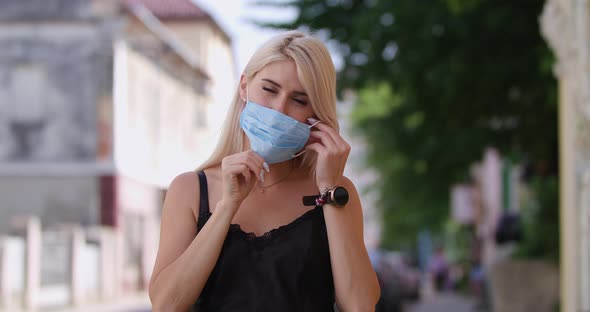 Attractive Young Blonde Woman Puts on a Protective Medical Mask and Looks Into the Camera