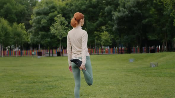 Back view of young woman do legs stretch after outdoor exercise.