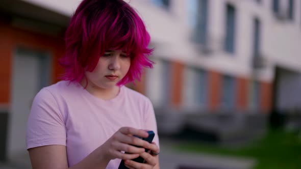 Chubby Teen Girl with Colored Pink Hair is Using Smartphone on City Street Portrait Social Media