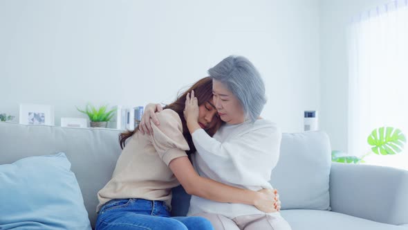 Asian loving elderly mother consoling and comforts upset daughter crying in tears for problem.