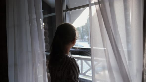 Happy Little Girl Opens the Curtains of the Window, Looking Outside the House. Smiling Watching