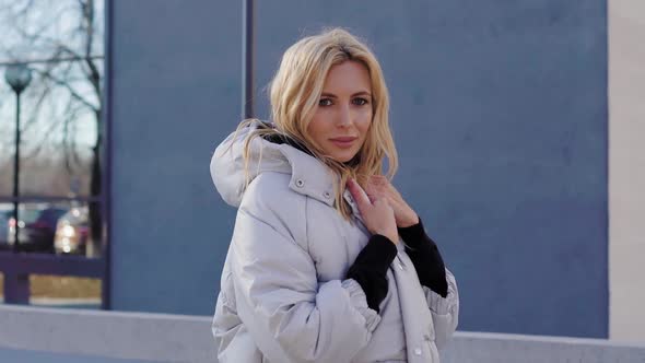 Beautiful Adult Blonde Woman Is Wearing Warm Trendy Down Jacket Standing Outdoors in City in Sunny