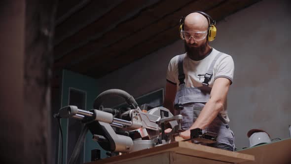 A Builder Cuts a Wooden Board on a Table Circular Saw in Construction Studio