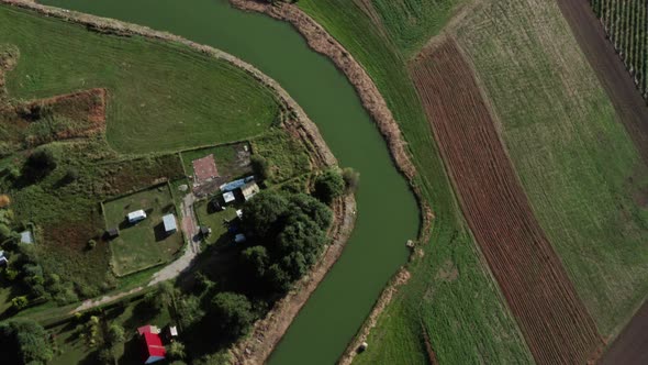 Aerial top down shot of a calm curvy river among the fields and farms of a small village.