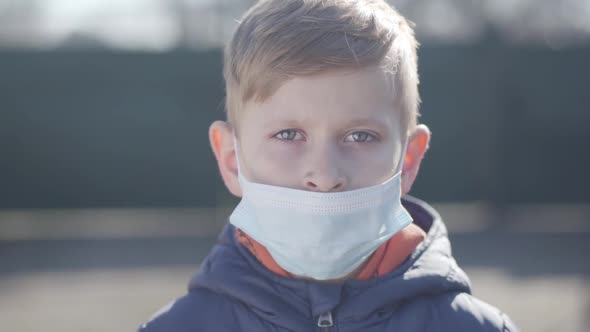 Portrait of Ill Blond Caucasian Boy in Face Mask Sneezing. Close-up Face of Sick Child with Red Eyes