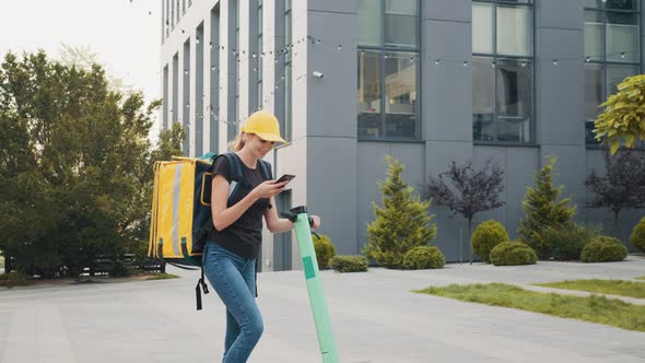 Delivery Woman Using Smartphone While Standing in the City with Electric Push