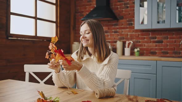 Young Woman is Weaving Decorative Wreath of Orange Autumn Leaves and Jute Thread