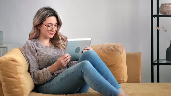 Excited Woman Talking Online Video Call on Tablet Pc Relaxing at Yellow Couch