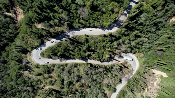 Downward droneshot of steep street in forest of Corfu, Greece. Cars and a bus driving as camera zoom