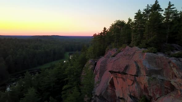 Aerial shot flying in front of a small forest covered cliff at sunset
