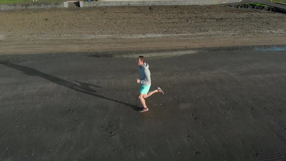 Aerial tracking shot of young man jogging on a beach in Auckland, New Zealand