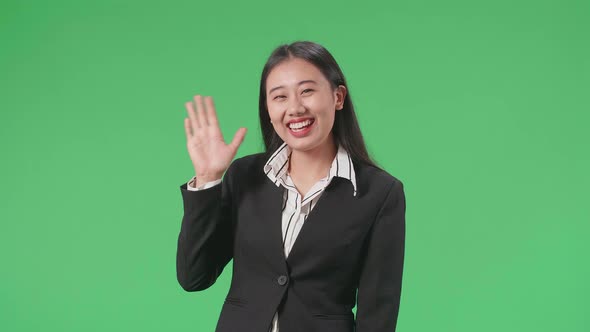 An Asian Business Woman Waving Hand And Smiling While Standing On Green Screen In The Studio