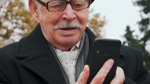 Close-up of a successful senior businessman using a smartphone in the park. Elderly man uses the app