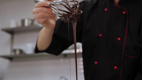 Closeup of a Chef's Hand Holding a Whisk with Liquid Chocolate