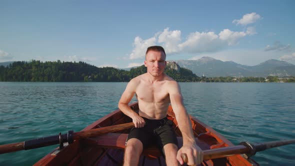 Young Man Controls Paddles in Wooden Boat on Bled Lake