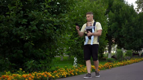 A Young Dad Walks with a Child Sitting in a Kangaroo Backpack