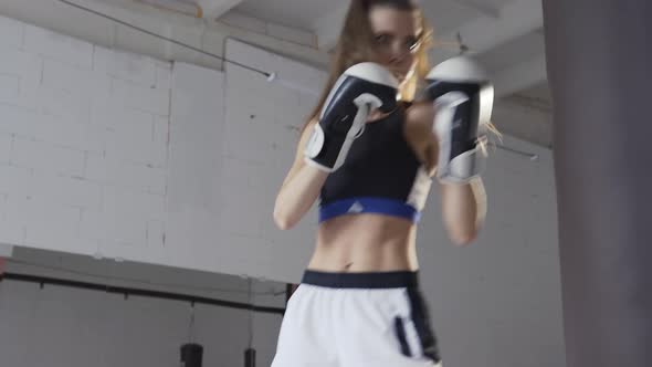 Female Athlete Boxing the Punching Bag in Urban Industrial Gym