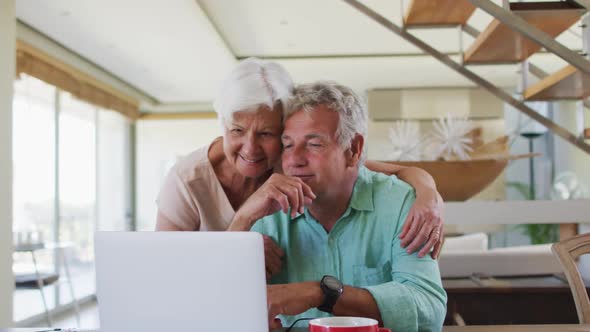 Happy senior caucasian couple talking to each other while using laptop together at home