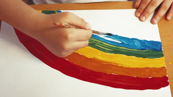 A Child's Hand Draws a Beautiful Rainbow with Colored Paints on a Sheet