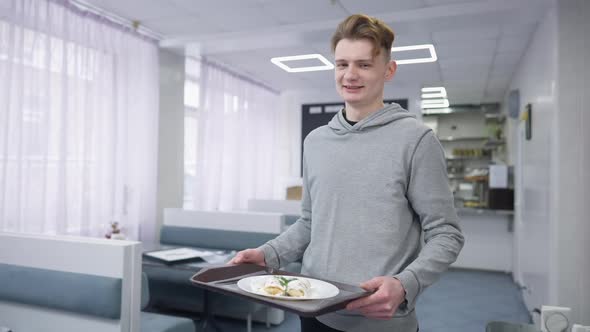 Portrait of Positive Young Man Posing with Dessert on Tray in Canteen Indoors