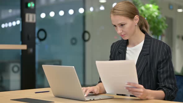 Beautiful Young Businesswoman Working on Laptop and Paperwork in Office