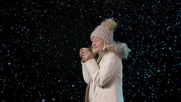 Side View of a Young Happy Blonde Enjoying the First Snow and Enjoying the Aroma of Hot Coffee