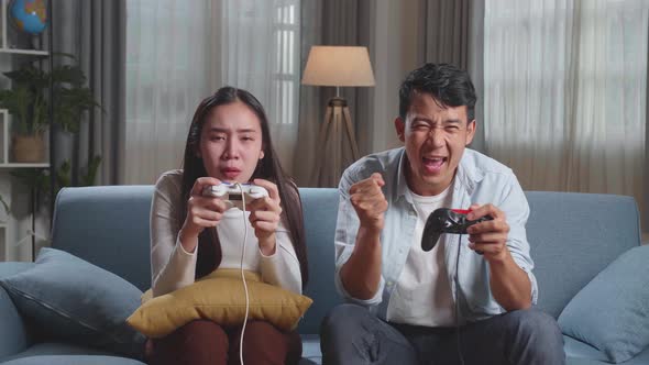 Asian Couple With Joystick Play Video Game On Tv, Male Celebrating Victory And Female Disappointed