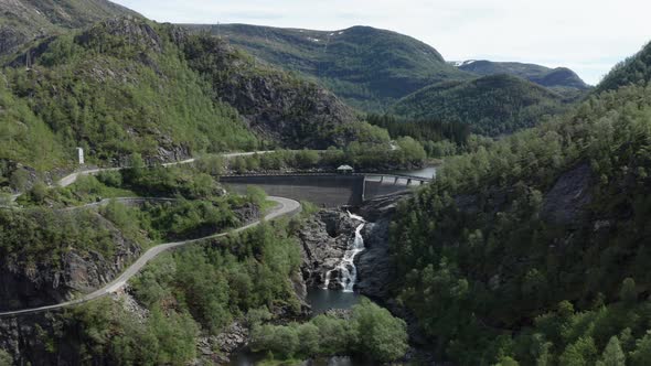 Aerial ascending shot over Dam with winding roads on valley of Norwegian Mountains