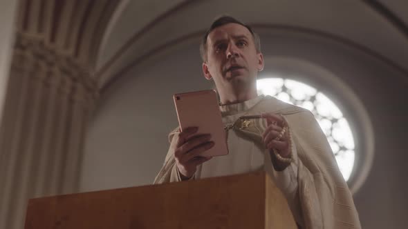 Clergyman Reading Prayer on Tablet PC during Mass