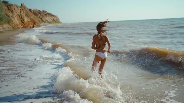 Happy Carefree Slender Woman with Beautiful Fitbody Running Along Seashore of Sea with Waves After