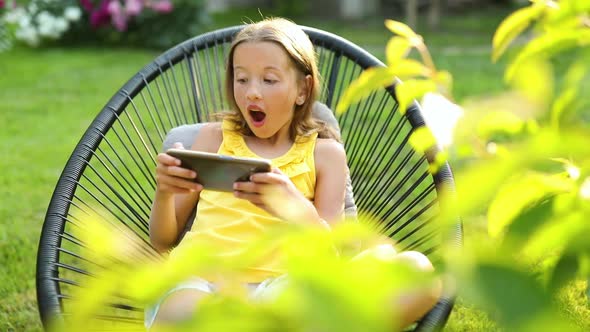 Happy kid girl playing game on mobile phone in the park outdoor