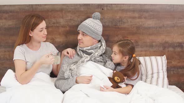 Sick Man with High Temperature Lying on Bed with Careful Child and Wife