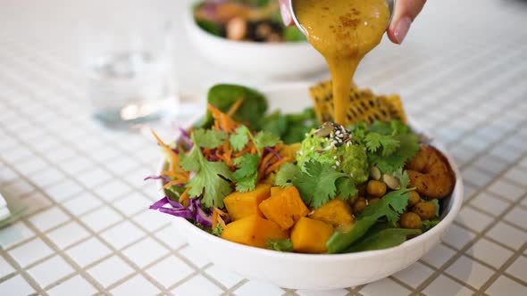 Woman Pours Sauce on Delicious Vegetarian Meal in Bowl