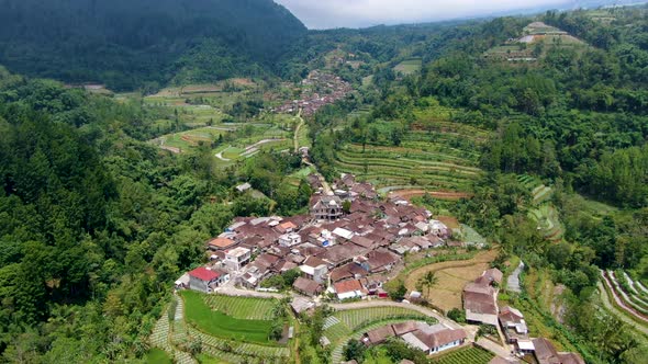 Small hillside village and farmland in Indonesian countryside aerial fly over