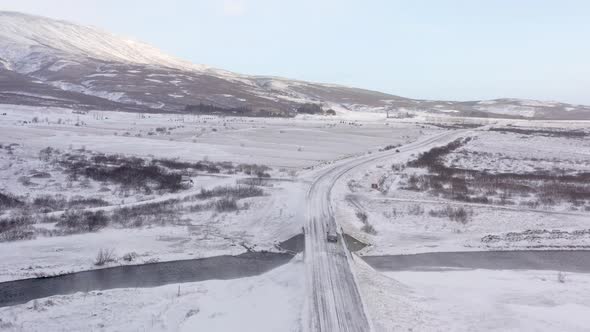 Aerial of Cars Driving on Winter Road next to River and Snow covered Forest - drone shot