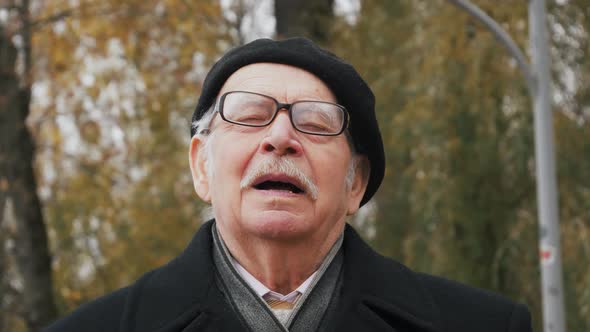 Handsome elderly senior taking deep breath. Old man relaxing breathing in fresh crisp air in park, s