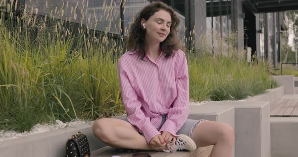 Fashionable white young woman listening to music by wireless earphones at Asian city suburban