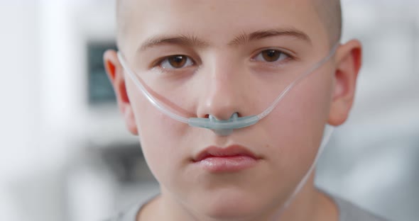 Close Up Portrait of Sad Sick Boy with Nasal Cannula Looking at Camera in Hospital