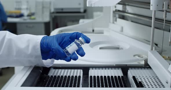 Crop View of Scientist Arm in Latex Glove Holding and Taking Glass Bottle with Vaccine