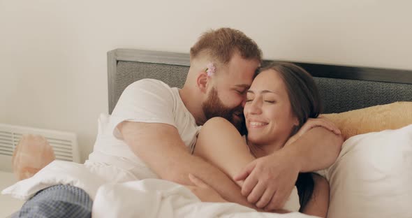 Happy Man and Woman Having Good Time and Playing Childish in Bed. Smiling Husband Whispering in Ear