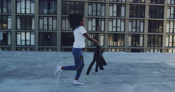 Fashionable young woman on urban rooftop running and throwing her jacket