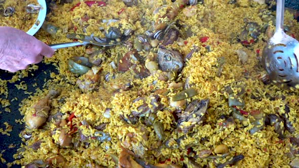 Top down shot of a traditional Spanish Paella  being scooped while one spoon tosses a piece of the