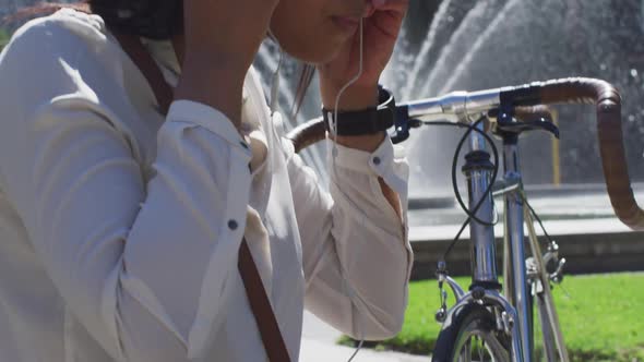 African american woman with bike putting earphones on in city park