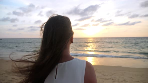 Woman with Long Hair Stands on Ocean Beach in Windy Evening