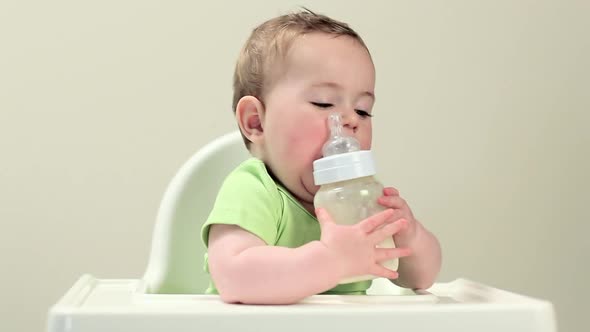 Baby boy sitting in highchair with bottle of milk