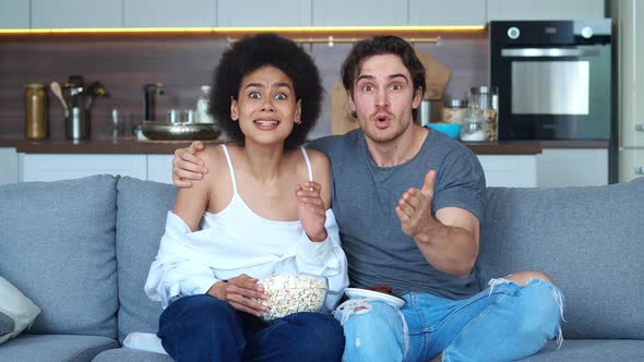 Excited Young Couple Caucasian Man and African American Woman Watching Football on TV at Home