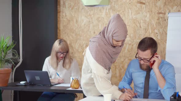 Arab Woman Is Talking with Colleague Man in Office, Correcting His Report